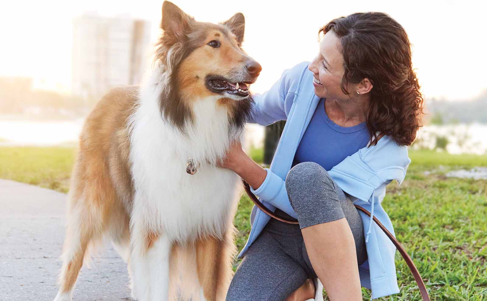 A woman kneeling down petting her dog and smiling.