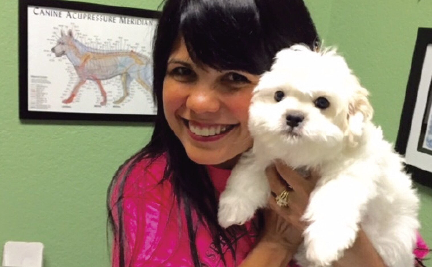 A woman smiles holding a small white dog closely.